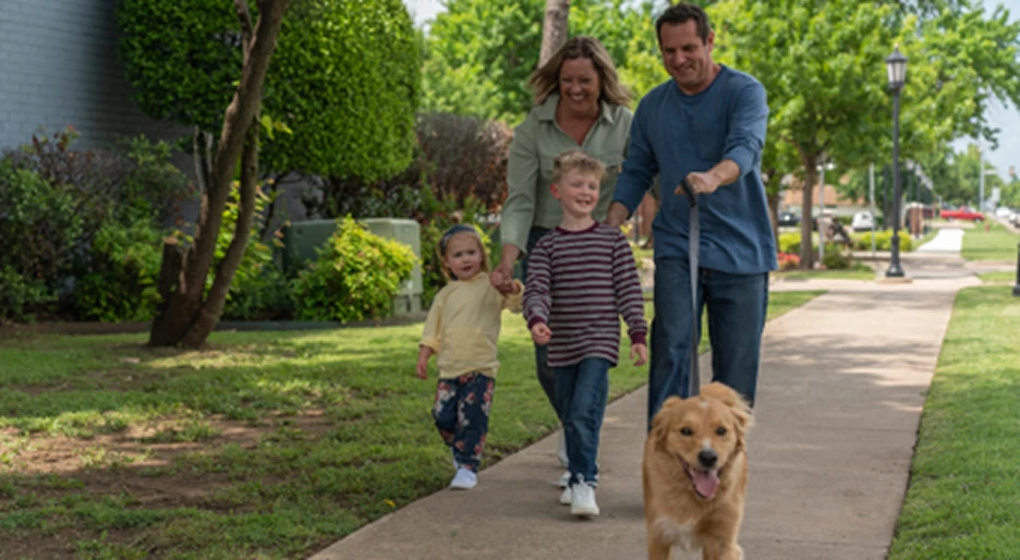 Family walking a golden retriever on a tree-lined sidewalk